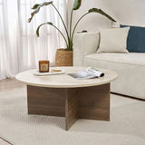 Runder Couchtisch mit Travertinplatte und dunklem Holzsockel in Kreuzform. Bank und Pflanze im Hintergrund.